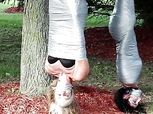 Two girls duct tape mummies outdoors